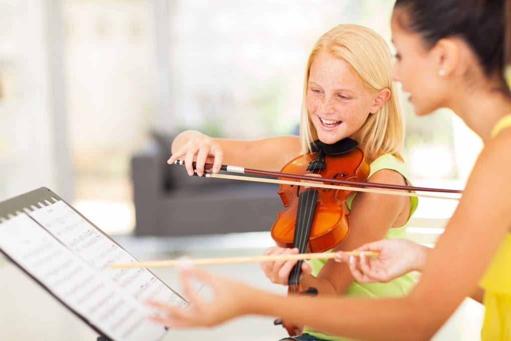 Child learning to play the violin with guidance from a nanny or private music tutor

